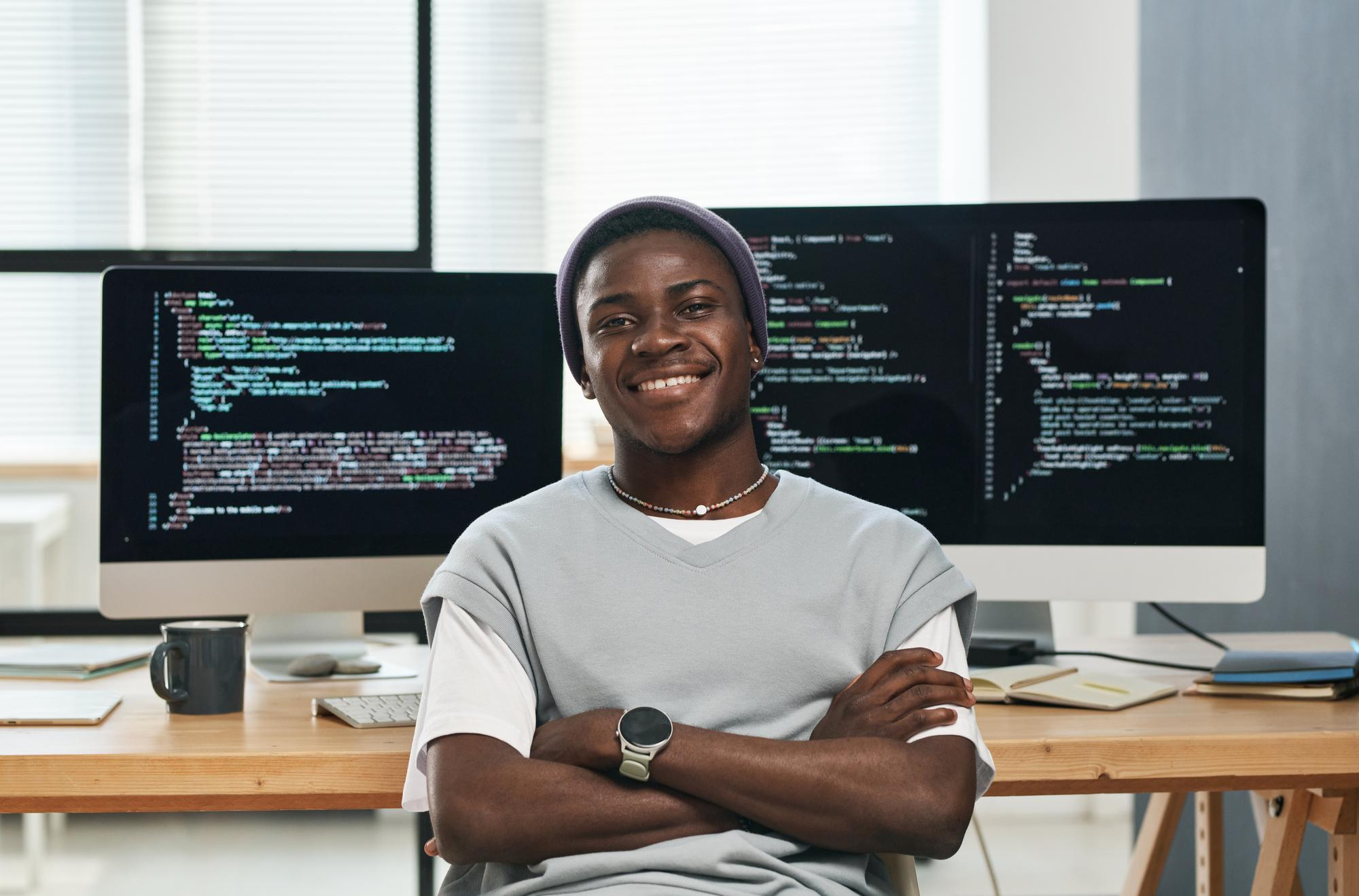 happy-young-successful-it-engineer-casualwear-looking-you-while-sitting-by-workplace-against-c happy-young-successful-it-engineer-casualwear-looking-you-while-sitting-by-workplace-against-c